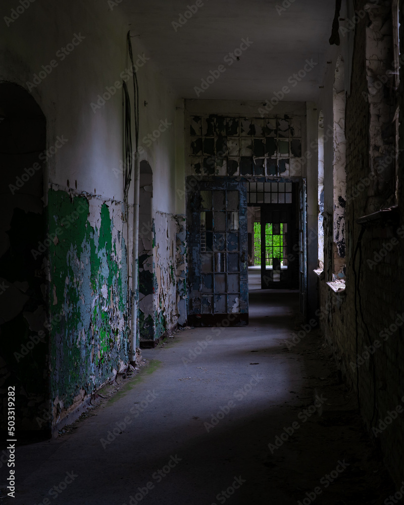 Fototapeta premium 10.05.2022- Oranienburg, Germany: Dark corridor of an abandoned German-Soviet lung hospital. Dilapidated walls, peeling paint, broken glass. Ruined tuberculosis-Sanatorium