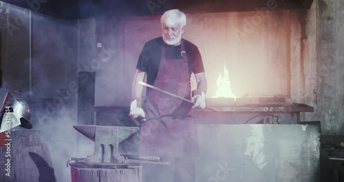 Side view of blacksmith long iron stick from open fire taking. Old strong male meatlwork with tongs holding, with hammer hard beating. Concept of forging and craftsmanship. photo