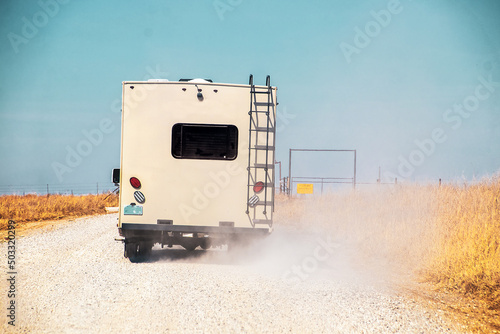 Camper driving on extremely dusty white gravel road through old metal gate with prairie to each side - dust grain photo