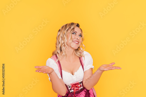 Woman in festive german dress spreads her arms to the sides in front of yellow background.