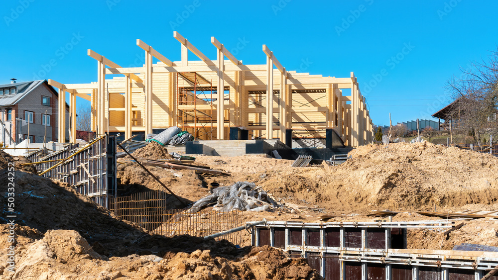 Fototapeta premium Construction site of a wooden house made of double profiled timber. The use of formwork when concreting the foundation of the fence. Building sand and sand-gravel mixture at the construction site.
