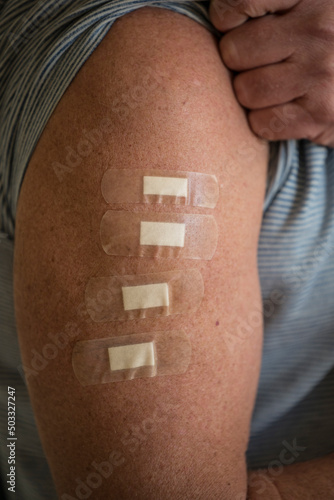 A man's arm with four bandaids, representing four innoculations, including a booster shot.