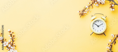 Spring background flowers. April floral nature and spring sakura blossom with alarm clock on soft yellow background. Banner for 8 march, Happy Easter with place for text. Springtime concept.