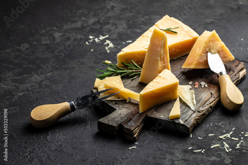 Parmesan cheese on a wooden board, Hard cheese, rosemary and cheese knife on a dark background. place for text, top view photo