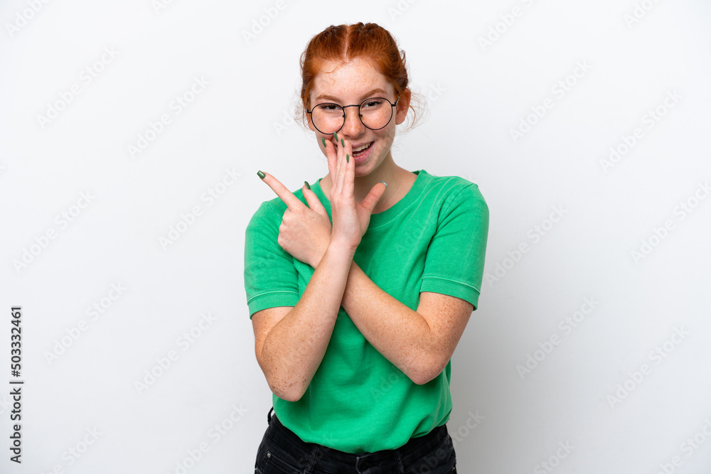 Young reddish woman isolated on white background pointing to the side to present a product and whispering something Young reddish woman isolated on white background pointing to the side to present a product and whispering something