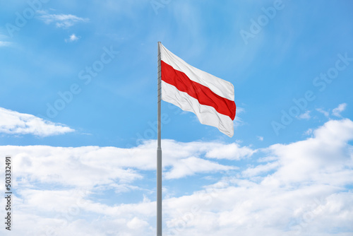 flag of protests in Belarus 2020. White-red-white historical flag of Republic of Belarus is waving in front of blue sky and clouds.