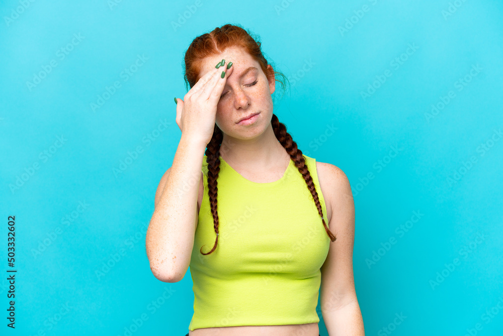 Young reddish woman isolated on blue background with headache