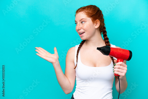 Young caucasian reddish holding a hairdryer isolated on blue background with surprise facial expression