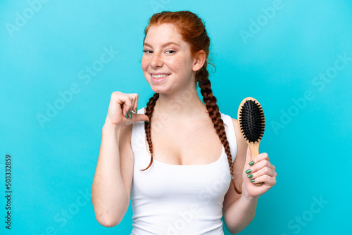 Young caucasian reddish woman with hair comb isolated on blue background proud and self-satisfied