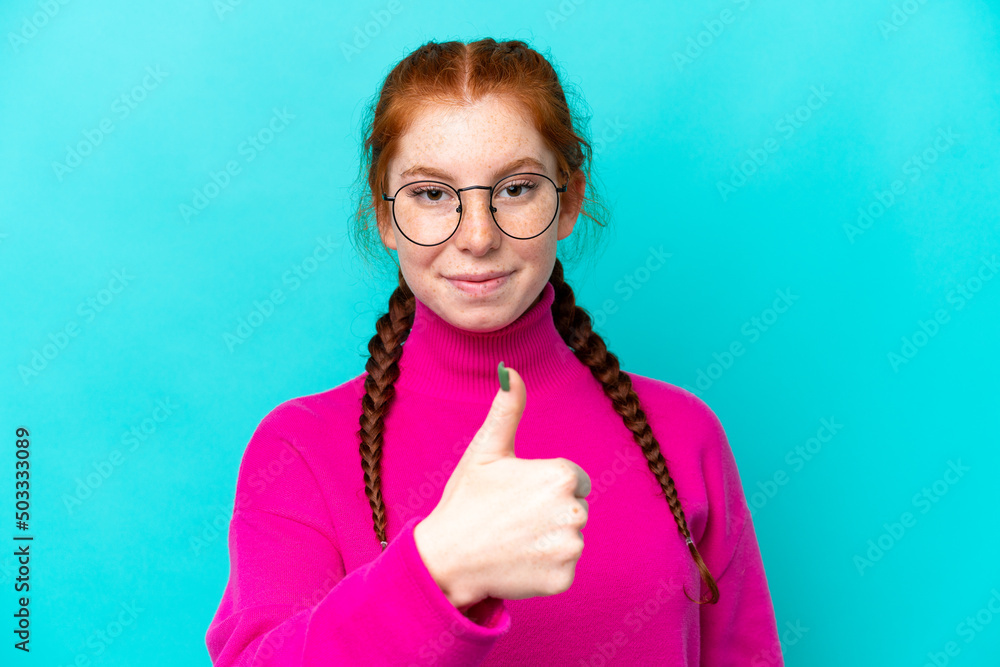 Young reddish woman isolated on blue background With glasses and with thumb up Young reddish woman isolated on blue background With glasses and with thumb up
