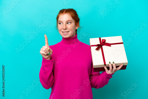 Young caucasian reddish woman holding a gift isolated on blue background intending to realizes the solution while lifting a finger up