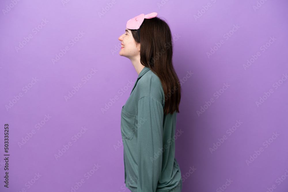 Young Russian woman in pajamas isolated on purple background laughing in lateral position Young Russian woman in pajamas isolated on purple background laughing in lateral position