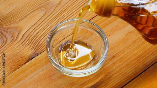 Pouring Oil Liquid. Oil is poured from a bottle into a cup. Olive oil pouring into a container on a wooden kitchen table. Crude palm oil being poured from the plastic bottle. Healthy sunflower oil