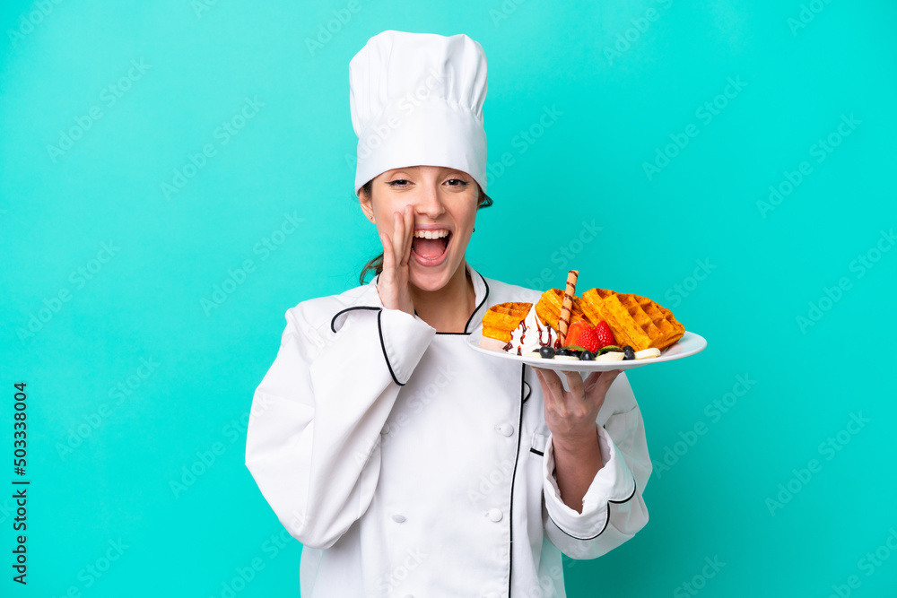 Young caucasian chef woman holding waffles isolated on blue background shouting with mouth wide open Young caucasian chef woman holding waffles isolated on blue background shouting with mouth wide open