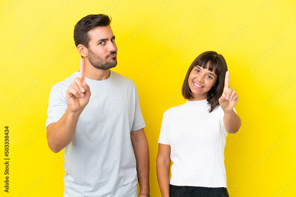 Young couple isolated on yellow background showing and lifting a finger Young couple isolated on yellow background showing and lifting a finger