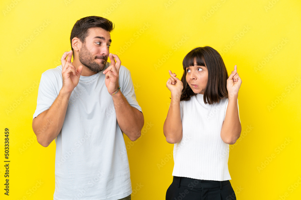 Young couple isolated on yellow background with fingers crossing and wishing the best Young couple isolated on yellow background with fingers crossing and wishing the best