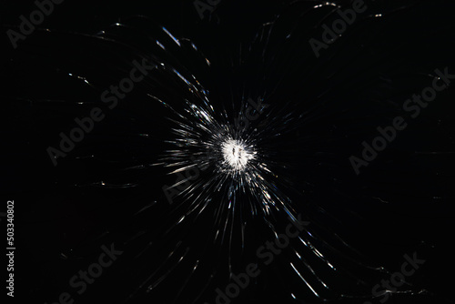 Cracks on a black glass background after a bullet shot. Armored glass after being hit by a bullet close-up