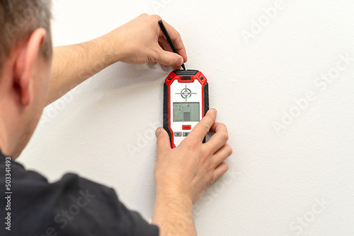Man using stud finder to locate framing studs located behind the walling surface. Using a wall scanner to identify hidden electrical wiring. Space for text