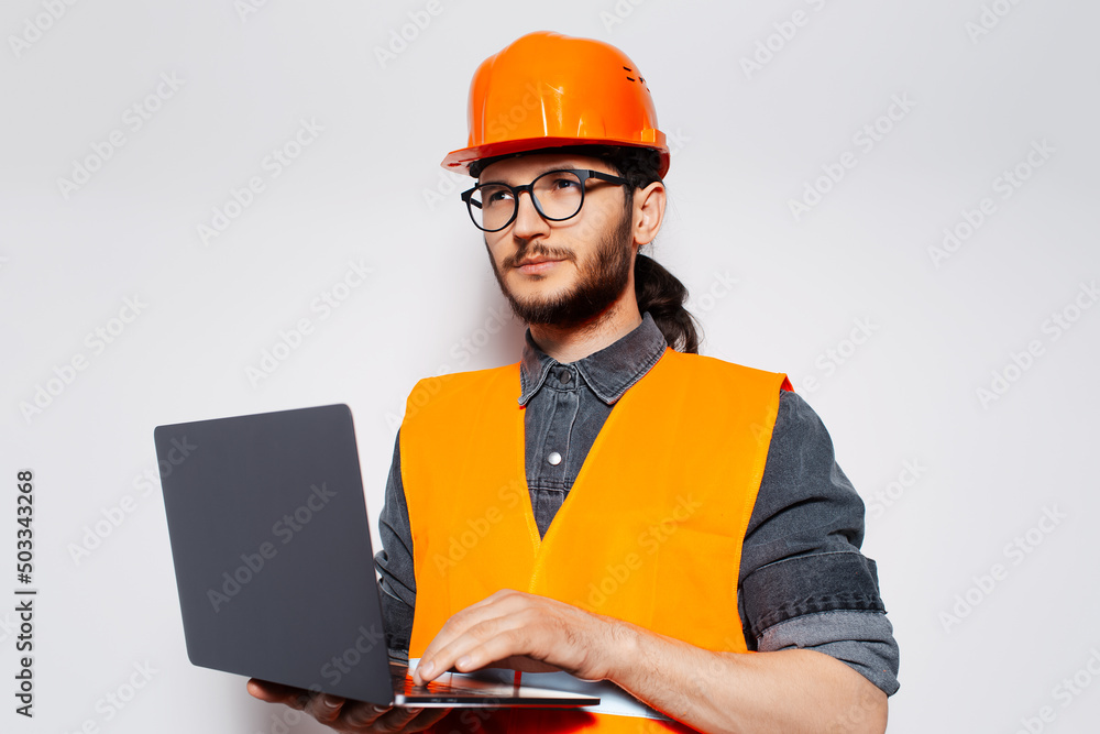 Studio portrait of engineer holding laptop in orange construction equipment.