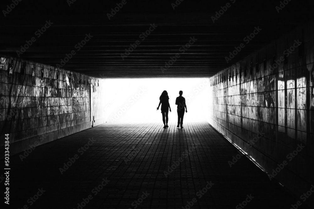 .black silhouettes of two people on an overexposed background in a dark room black and white photo