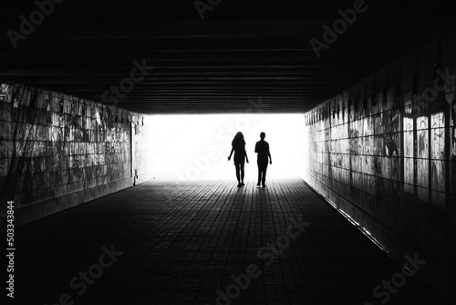 .black silhouettes of two people on an overexposed background in a dark room black and white photo