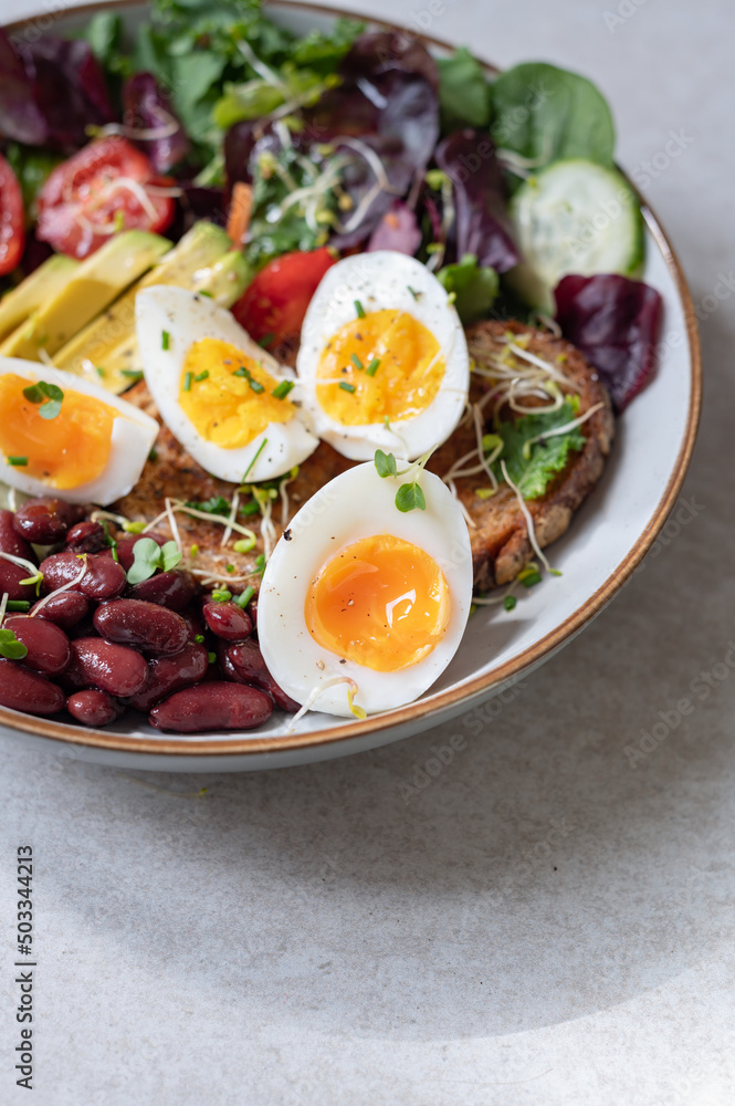 Light green salad with leaves, avocado, cherry tomatoes, cucumber slices, red beans, micro greens and medium boiled eggs on slice of toasted bread. Light green salad with leaves, avocado, cherry tomatoes, cucumber slices, red beans, micro greens and medium boiled eggs on slice of toasted bread.