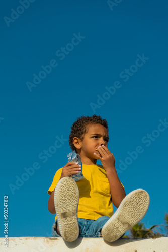 Black boy eating a cookie with chocolate. Dressed in yellow t-shirt, African American boy © TxemaPhoto