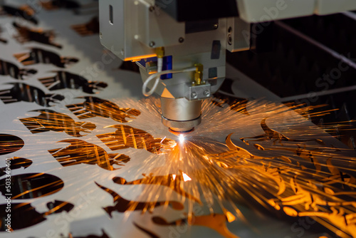 Automatic cnc laser cutting machine working with sheet metal with many orange sparks at factory, plant. Metalworking, industrial, manufacturing, technology and equipment concept