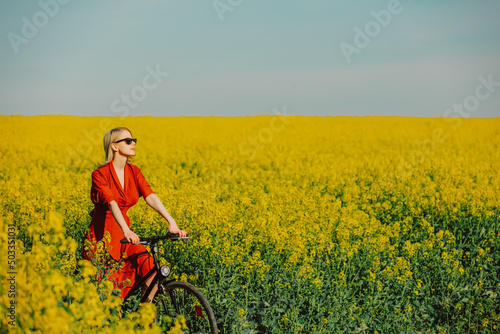  girl in vintage dress and sunglasses with bicycle in rapeseed field