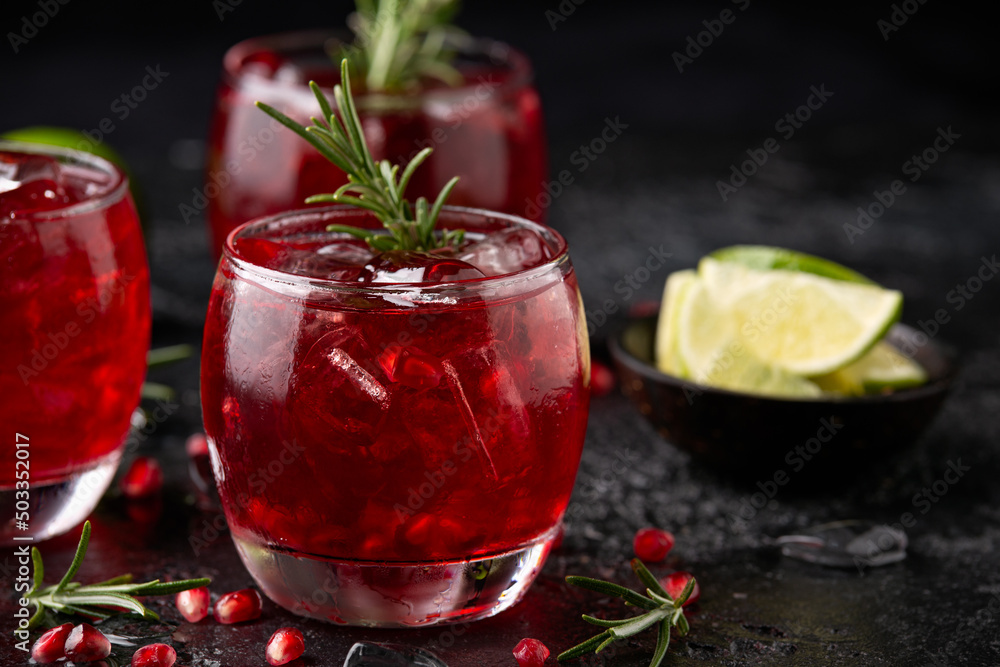 Pomegranate gin cocktail with lime, rosemary and ice on rustic black table Pomegranate gin cocktail with lime, rosemary and ice on rustic black table