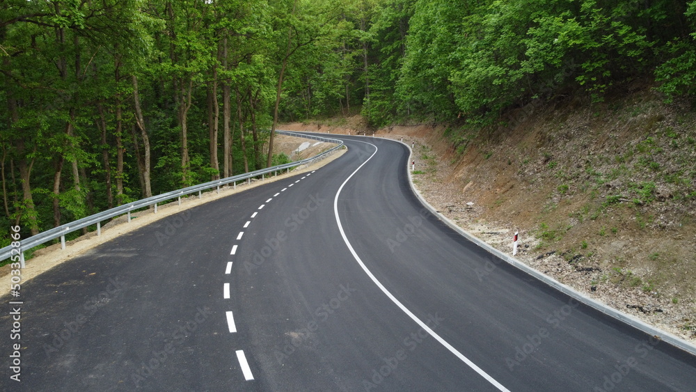 Aerial shot of a winding road passing through a beautiful dense green forest Aerial shot of a winding road passing through a beautiful dense green forest
