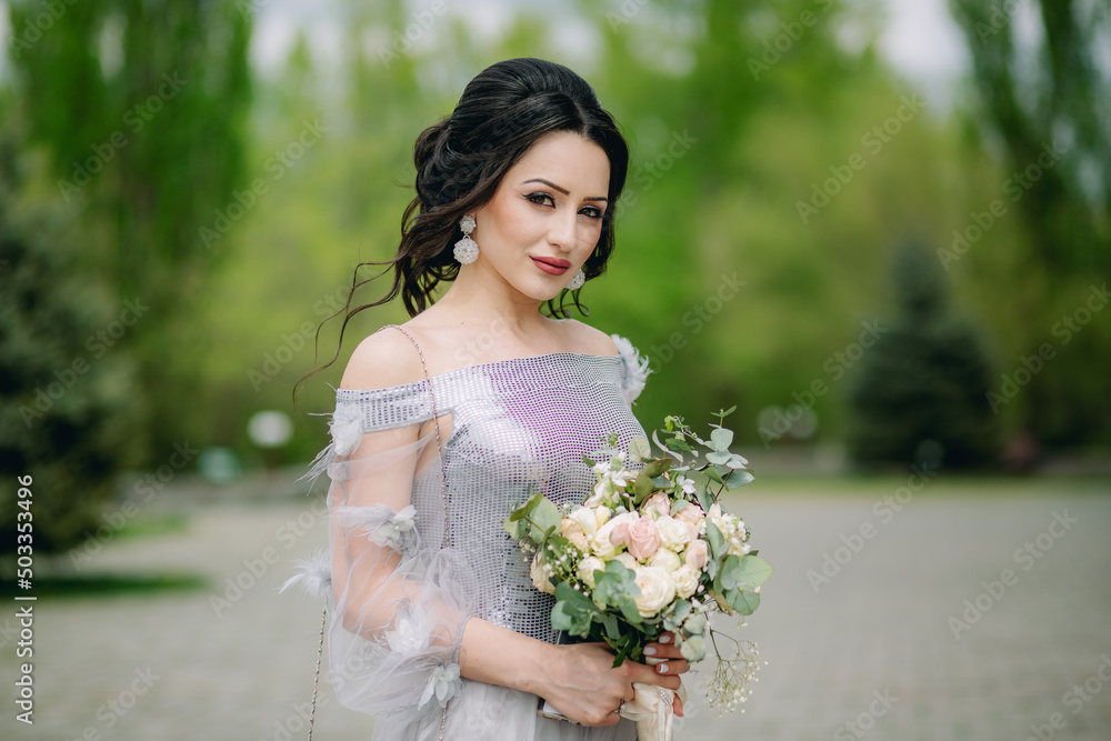 Cute and smiling bridesmaid holding bridal bouquet in front of blurred natural green background and looking at camera