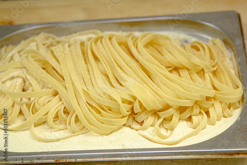 The pasta  cut into long strips  lies on a wooden tray. Use your hands to stir the raw pasta for cooking.