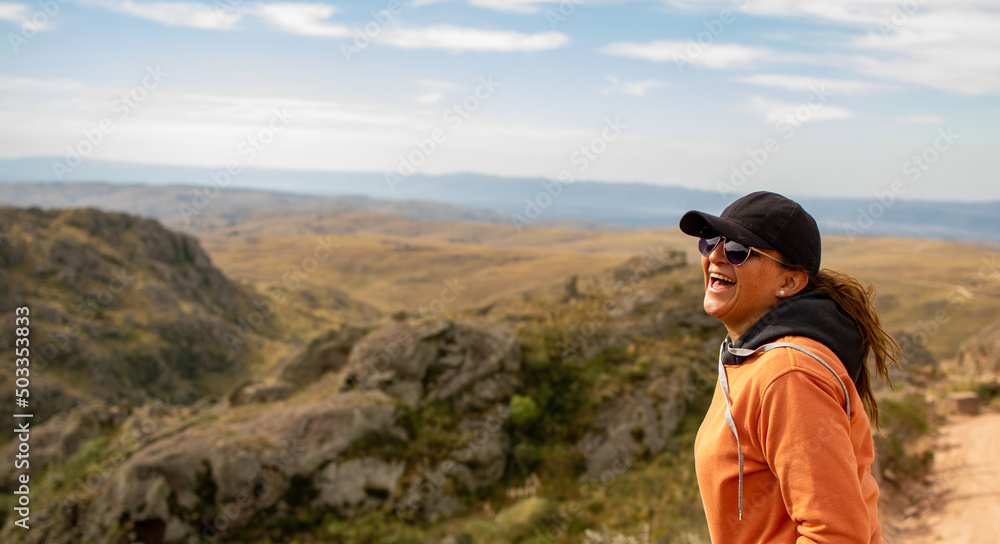 Portrait of latin woman dressed in orange with a cap and tail in the back having fun during the day of trekking in the mountain forest - laughing out loud