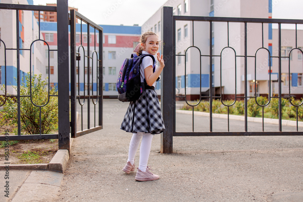 Back to school. Girl in school uniform go to school with backpack behind their backs. Kid waving her hand saying bye. Beginning of lessons. First day of autumn. Elementary school student. Back to school. Girl in school uniform go to school with backpack behind their backs. Kid waving her hand saying bye. Beginning of lessons. First day of autumn. Elementary school student.