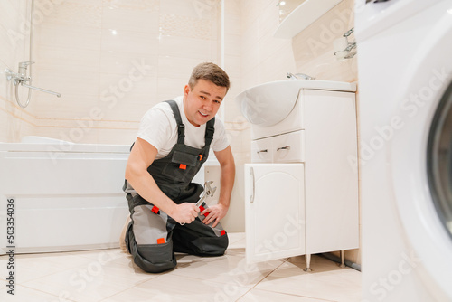 A male plumber repairs siphon under the sink in the bathroom.
