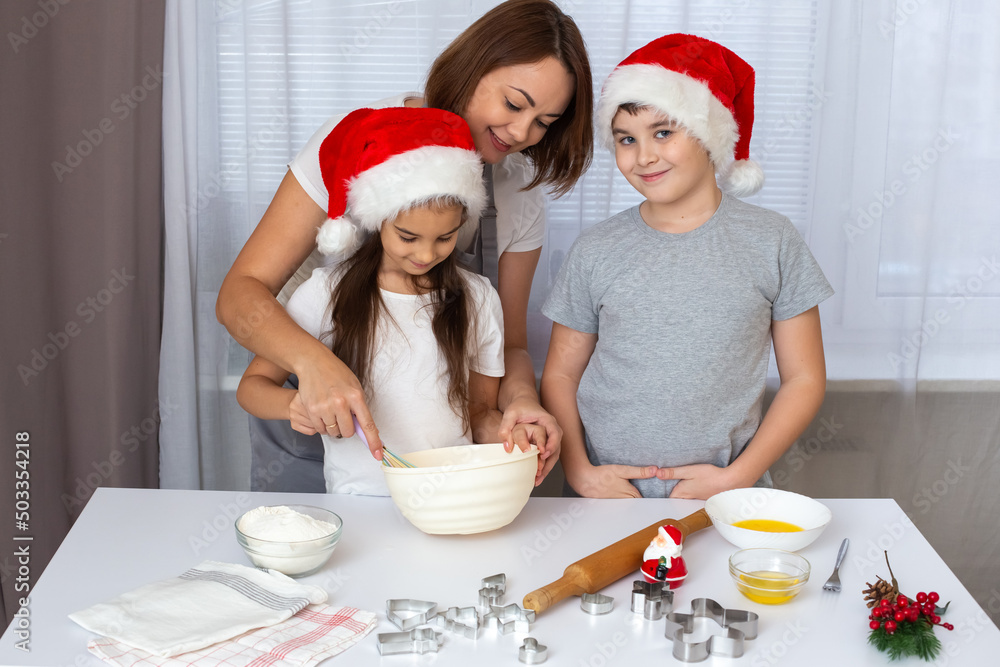 mom and children in red caps cooking Christmas cookies in the kitchen. mom and children in red caps cooking Christmas cookies in the kitchen.