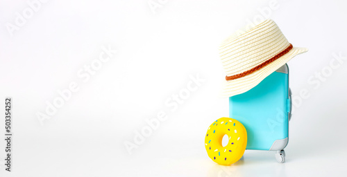 Wallpaper Mural A blue suitcase on wheels, a straw hat, and a yellow inflatable donut stand on a white background. Torontodigital.ca