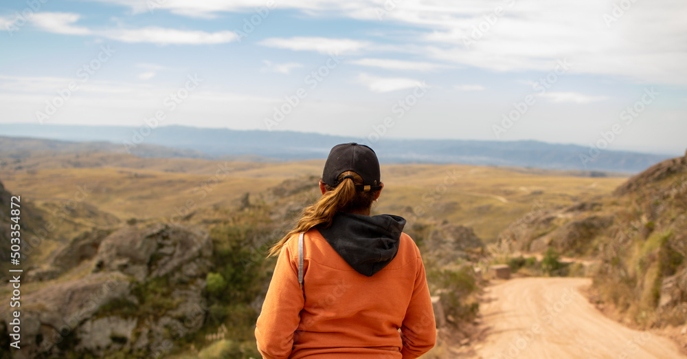 Portrait of latin woman dressed in orange with a cap and tail turned back having fun during the day of trekking in the mountain forest - Focus from the back