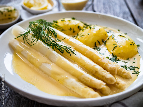 White boiled asparagus in hollandaise sauce with potato puree served on wooden black table
 photo