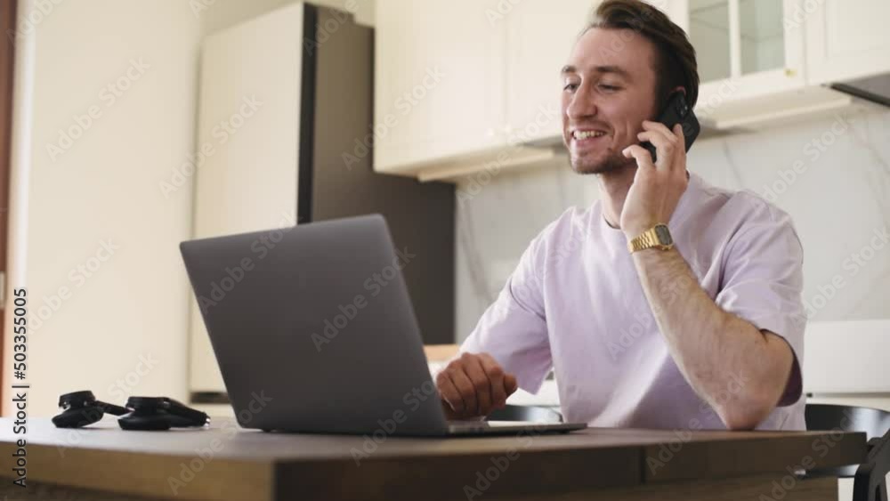 Concept of a man at laptop in casual cloth at home workplace makes a call to the client from working at home and confirming the deal by phone call. Concept of a man at laptop in casual cloth at home workplace makes a call to the client from working at home and confirming the deal by phone call.