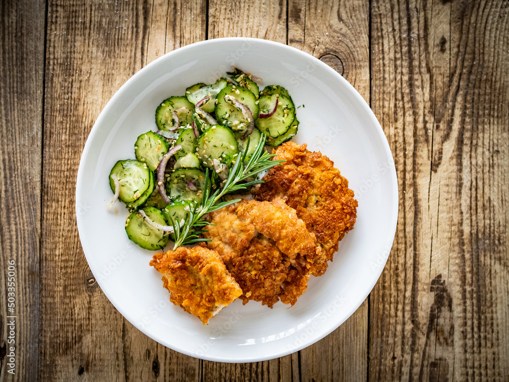 Breaded fried pork chop with sliced cucumbers and rosemary on wooden table
Breaded fried pork chop with sliced cucumbers and rosemary on wooden table