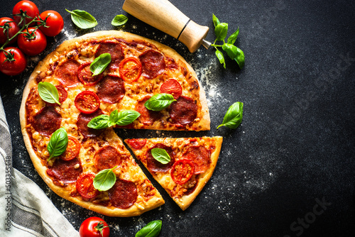 Pizza with salami cheese, tomatoes and basil on black table. Top view with copy space.