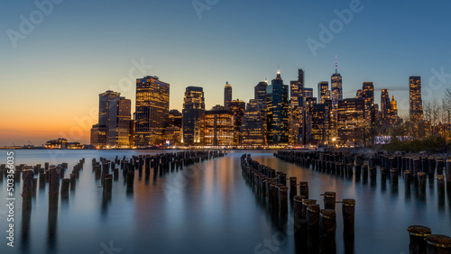 New York  USA - April 25  2022  Long exposure of the Lower Manhattan skyline at sunset with an old Brooklyn pier in the foreground