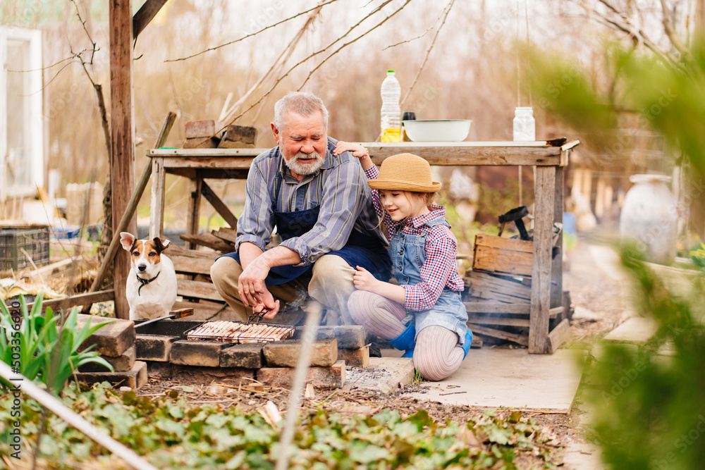 granddaughter helps grandfather with dog cook barbecue on the grill, bonfire granddaughter helps grandfather with dog cook barbecue on the grill, bonfire