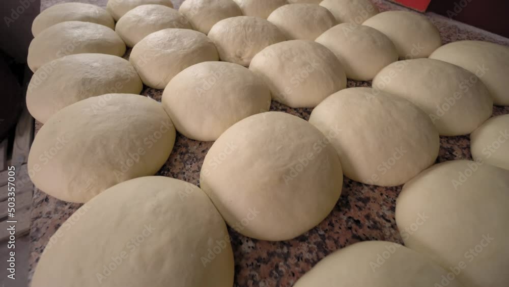 Close-up of finished pink dough in bakery on wooden table. Workflow. Private bakery. Bread production. Dough is divided into round buns and is waiting to be placed in oven. Close-up of finished pink dough in bakery on wooden table. Workflow. Private bakery. Bread production. Dough is divided into round buns and is waiting to be placed in oven.