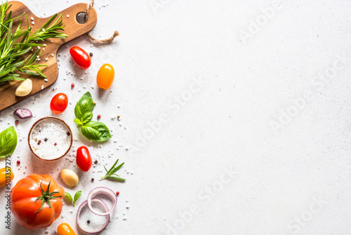 Food cooking background on white kitchen table. Fresh vegetables, herbs and spices with wooden cutting board. Top view with copy space.