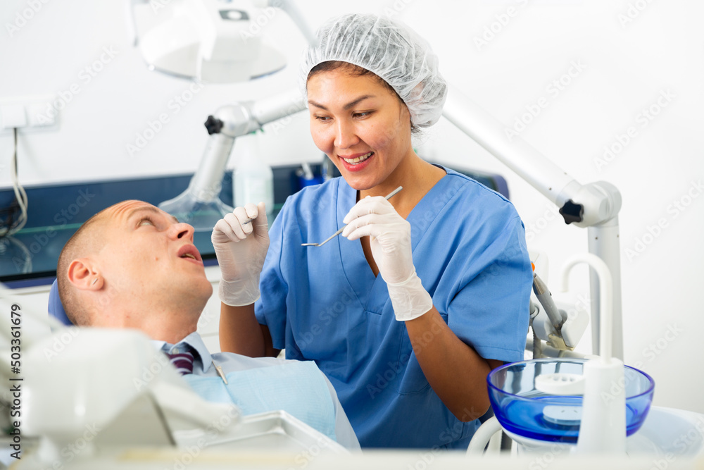 Fototapeta premium Young man patient who came to an appointment with a female dentist is sitting in a dental chair in the clinic office