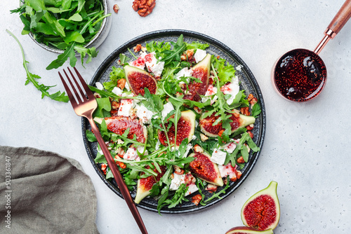 Delicious summer salad with sweet figs, white feta cheese, walnuts, arugula and jam vinegar dressing on white table background, top view, negative space