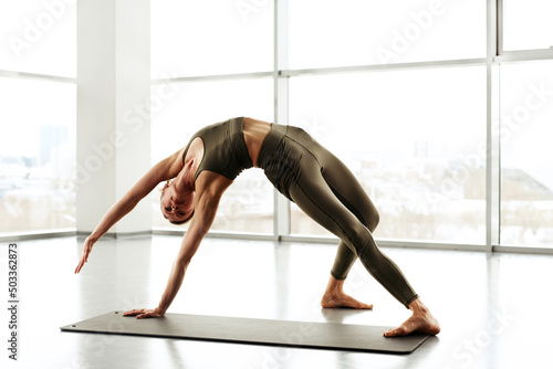 Strong young woman in leggings raising arm and twisting body in bridge position